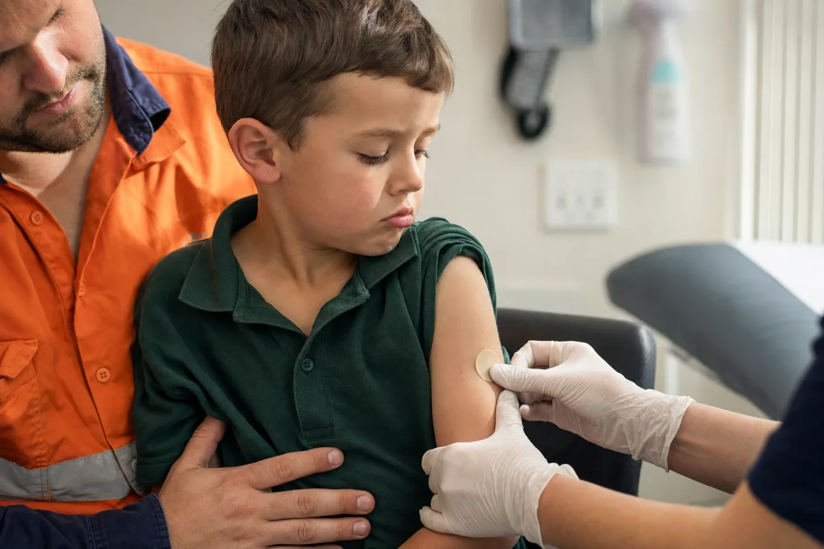 A boy on his dad's lap checking the plaster on his arm after an immunisation